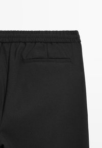 Pantaloni neri con elastico in vita, dotati di una tasca posteriore e di un tessuto texturizzato. Il design enfatizza comfort e praticità.