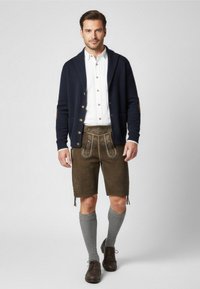 Traditionele mannenoutfit met een marineblauwe cardigan, een witte overhemd, bruine leren korte broek met geborduurde details, grijze kniekousen en donkere schoenen.