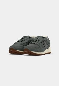 Grå ruskinds- og mesh-sneakers har en tekstureret overflade, rund tå, snørebåndslukning og en kontrasterende hvid mellemsål med en brun gummi ydersål.