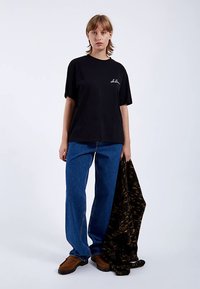 Musta puuvillainen t-paita, jossa on lyhyet hihat ja käsinkirjoitettu valkoinen logo. Yhdistetty suoralahkeisiin sinisiin farkkuihin ja ruskeisiin kenkiin.