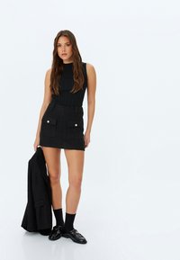 Top sin mangas de canalé negro combinado con una mini falda de tweed negro con dos bolsillos frontales y acentos dorados, complementado con unos mocasines negros y calcetines.