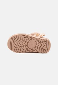 Suela de una bota de color marrón claro, con un patrón de textura en la suela que presenta diseños en zigzag y florales para mejorar la tracción. Acento de piel suave cerca del talón.