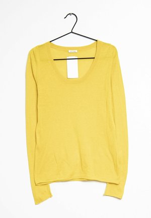 Żółty sweter z długim rękawem i okrągłym dekoltem, wiszący na czarnym wieszaku na ubrania na białym tle, z przymocowaną białą metką cenową.