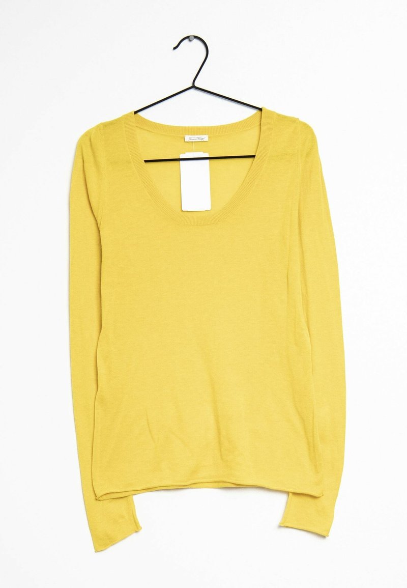 Żółty sweter z długim rękawem i okrągłym dekoltem, wiszący na czarnym wieszaku na ubrania na białym tle, z przymocowaną białą metką cenową.