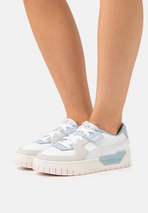 Baskets blanches et bleu clair avec un cuir lisse, une languette en maille ventilée et une semelle en caoutchouc rose pâle texturée. Logo PUMA sur le côté.