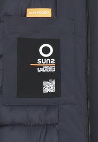 Interno di una giacca a vento di colore blu scuro con un'etichetta in tessuto nera che presenta un logo bianco, un codice QR e un'etichetta arancione "Safe Pocket" sopra.