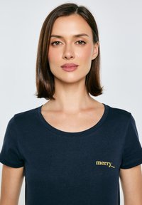 Námořnická modrá tričko vyrobené z bavlny, s kulatým výstřihem a krátkými rukávy, s zlatou výšivkou slova "merry" na prsou.