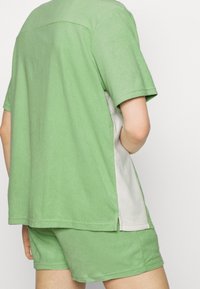 Camisa de algodón verde de manga corta con un panel lateral gris claro, con un corte relajado y un dobladillo recto, combinada con pantalones cortos a juego.