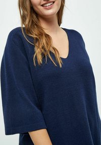 Dunkelblauer V-Ausschnitt-Pullover aus weichem Garn, mit kurzen Ärmeln und lässiger Passform, der eine glatte Textur und ein minimalistisches Design aufweist.