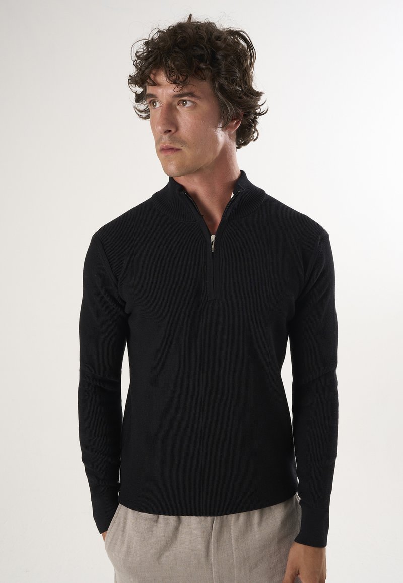 Must mustribal pullover, millel lukk, pikkade varrukatega ja sobiva disainiga. Kanda heledate pükste peal.