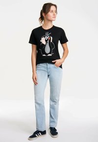 Black cotton t-shirt featuring a cartoon penguin design in white, gray, and orange. Pair of light blue jeans and black sneakers visible.
