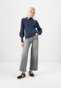 Navy ribbed sweater with puffed sleeves, paired with gray wide-leg jeans and black sneakers featuring a white logo and beige laces.