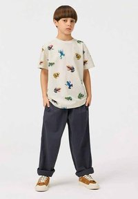 Kortærmet creme t-shirt med farverige dyretryk, parret med mørkegrå afslappede bukser og lysebrune sneakers.