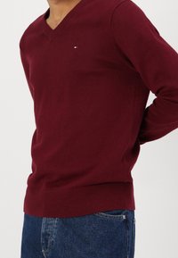 Pull col en V bordeaux en tissu tricoté, avec un petit logo sur la poitrine gauche, de coupe ajustée et doté de poignets et d'un ourlet côtelés.