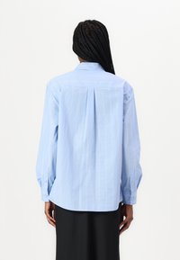 Light blue long-sleeve shirt with vertical white stripes, tailored fit, button-down collar, and pleat detailing at the back.