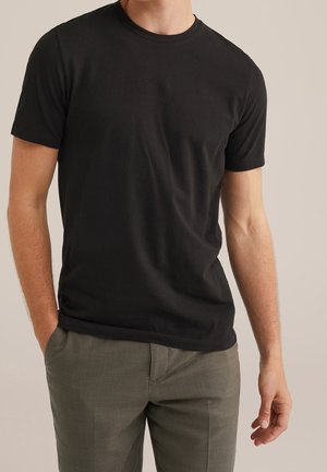 Sort kortærmet t-shirt lavet af bomuld med rund halsudskæring, strømlinet pasform og glat tekstur, kombineret med grå bukser.