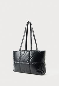 Sac fourre-tout noir matelassé avec de longues poignées doubles et un design rectangulaire rembourré sur fond blanc.