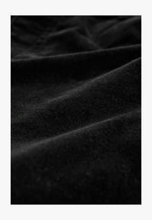 Juodas audinys su minkšta, tekstūruota paviršiumi, pabrėžiančiu subtilius bangas ir raukšles, turintis aksominį išvaizdą ir vienodinę spalvą.