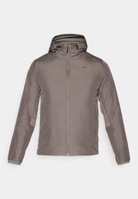 Nike-jacka, lätt, gråbrun, med huva, hel dragkedja, långa ärmar, kontrasterande paneler och en liten logotyp på bröstet.