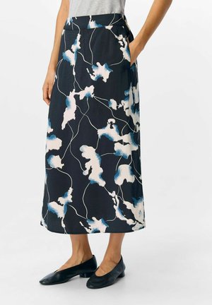 Jupe longue et sombre avec un motif floral en blanc et différentes nuances de bleu, dotée de poches latérales et d'une texture lisse. Associée à des ballerines noires.