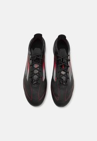 Black athletic shoes with red accents, featuring a textured upper, striped pattern on the sides, and a sleek, streamlined design.