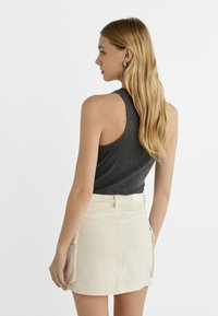 Sivo rebrasto tank top, usklađen s kremasto-belimi šortsem sa stransko žepom in prilegajočim pasom, gledano zadaj.