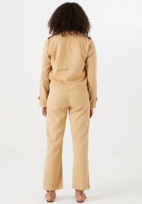 Beżowa bawełniana kurtka o lekko skróconym kroju, zestawiona z szerokimi beżowymi spodniami. Materiał wydaje się gładki i ma luźny krój.