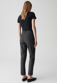 Zwart kortekorte mouwen top gecombineerd met grijs geruite broek. De broek heeft een rechte snit en opgerolde broekspijpen. Simpele zwarte flats gedragen.