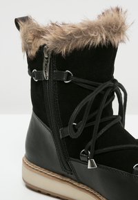 Botín negro con ribete de pelo sintético, materiales de cuero y ante, cierre de cremallera y cordones decorativos. Cuenta con una suela de goma con un ligero tacón.