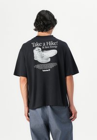 Black oversized t-shirt featuring a graphic print of boots and text on the back. Short sleeves, relaxed fit, and cotton material.