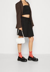 Svart kort topp, svart kjol med dragsko, brun oversized blazer, röda strumpor, svarta platå loafers och en vit handväska.