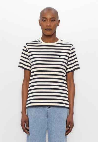 T-shirt rayé bleu marine et crème en coton avec un col rond, des manches courtes et un petit logo sur la poitrine. Coupe décontractée.