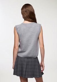 Maglione senza maniche grigio a maglia con bordi a costine, indossato sopra una gonna a pieghe grigia a scacchi, che mette in mostra una texture liscia e un design semplice.
