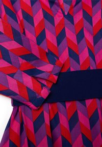 Buntes Kleid mit einem geometrischen Muster aus roten, rosa und marineblauen Chevron-Streifen. Mit einem marineblauen gerippten Taillenbund und gefalteten Manschetten.