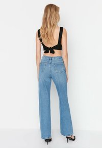 Top negro corto con detalle de lazo en la espalda, combinado con pantalones vaqueros de pierna ancha en azul claro, que presentan bolsillos clásicos y una textura de denim.
