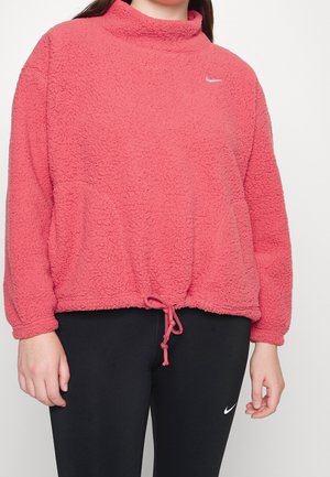 Personne portant un pull polaire rose avec cordon de serrage à l'ourlet et des leggings noirs, tous deux arborant de petits logos Nike blancs.