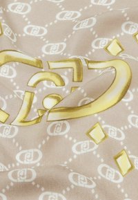 Bufanda de seda con fondo beige y diseños geométricos en blanco y dorado, que incluyen patrones interconectados y formas de diamante. Textura suave.