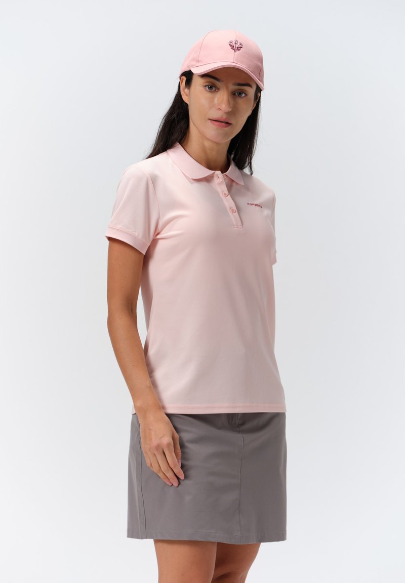 Vaaleanpunainen poolopaita, jossa on kaulus ja lyhyet hihat, yhdistettynä harmaisiin hameeseen. Hatussa on vastaava vaaleanpunainen kukkakuosi.