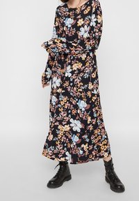 Svart långärmad klänning med ett blommönster i nyanser av rosa, blått och gult; mjukt, flödande tyg; matchad med svarta kängor.