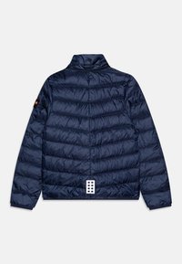 Tengerészkék puffermellény magas gallérral, vízszintesen steppelt textúrával és hat kerek lyukat tartalmazó patentos záródással a hátsó részen.