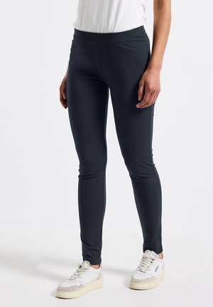 Zwarte leggings van rekbaar materiaal met een gladde textuur, voorzien van een hoge tailleband en een skinny fit, gecombineerd met witte en grijze sneakers.