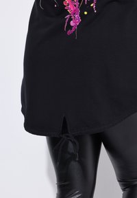 Túnica negra de algodón con un diseño de estampado floral en rosa y amarillo. Dobladillo curvado con detalle de cordón.