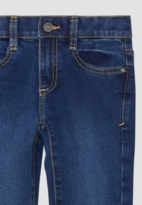 Tmavě modré džíny z denimu s pěti kapsami, žlutým prošíváním a zapínáním na předním knoflíku. Hladká textura s klasickým střihem.