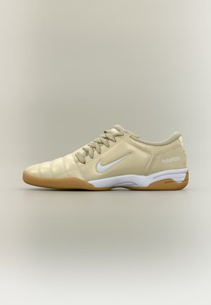 Chaussure de football en salle beige avec un swoosh Nike blanc, semelle en gomme, lacets et texte "total90 III" au talon, vue de côté.
