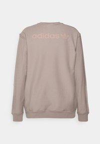 Sudadera marrón con cuello redondo y mangas largas. Presenta detalles desgastados en los hombros y un logotipo de Adidas en rosa claro en la parte posterior.