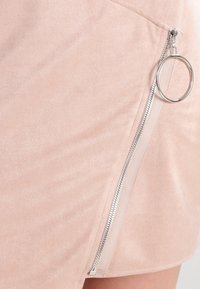 Svetle růžová sukně z faux semiše s bočním zipem s stříbrným kolečkem na tahání a hladkým povrchem. Jednoduchý rovný střih, nezdobená.