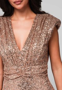 Abito in paillettes rosa dorato con scollatura a V profonda e maniche corte a pieghe, caratterizzato da una vita aderente e una superficie lucente.
