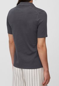 Person som bär en mörkgrå kortärmad pikétröja och vita byxor med vertikala svarta ränder, sedd bakifrån.