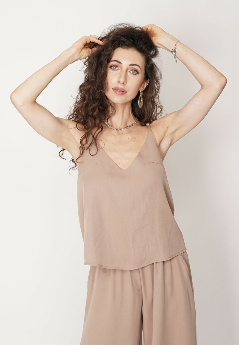 Beżowy, bezrękawnik z dekoltem w szpic, wykonany z miękkiej tkaniny. Charakteryzuje się luźnym krojem i delikatnym marszczeniem.