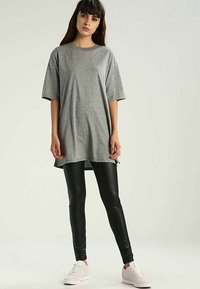 Grå oversized t-shirt med korta ärmar, tillverkad av mjukt tyg, kombinerad med svarta leggings och ljusa skor. Enkel, avslappnad look.